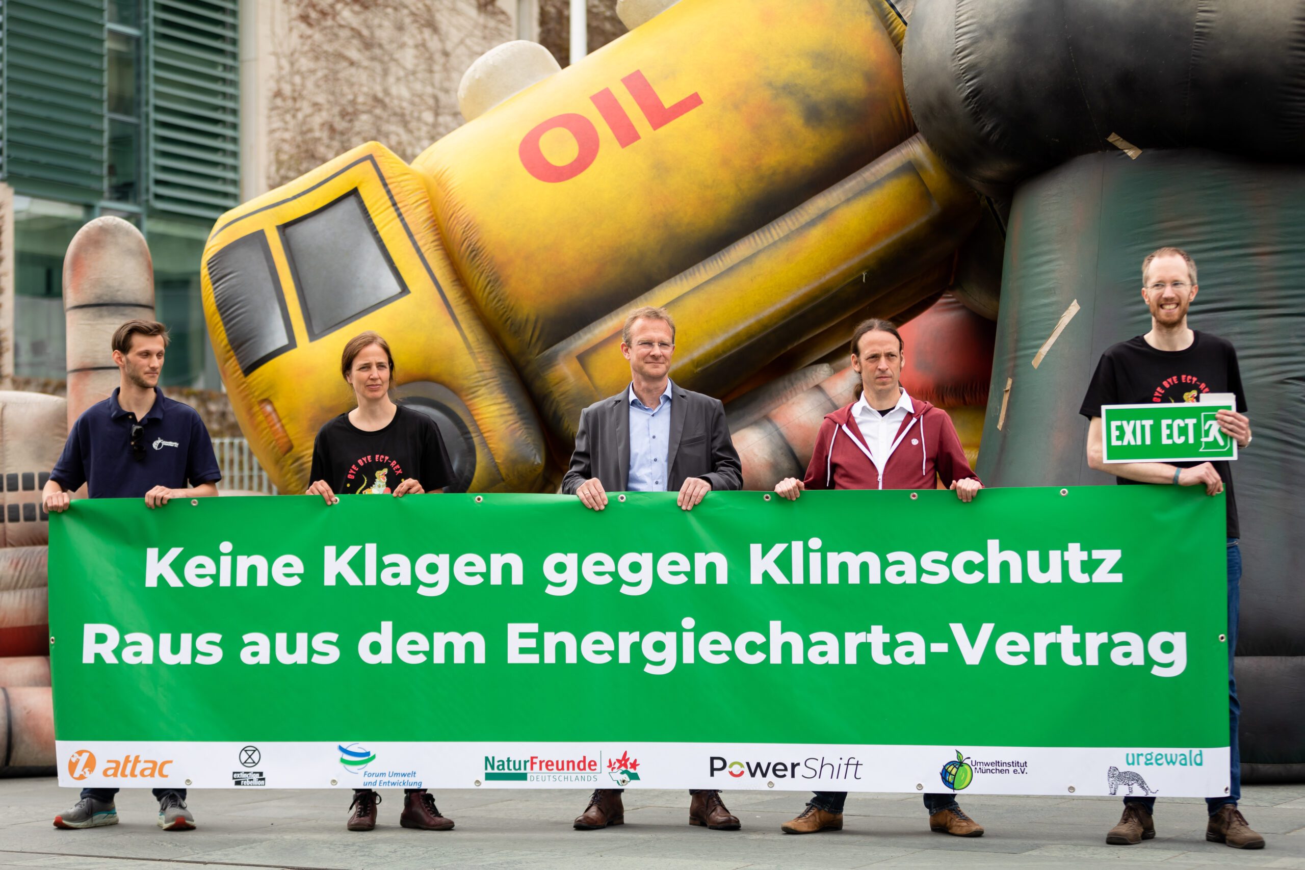 Fünf Menschen stehen vor einem Plakat, mit der Aufschrift "Keine Klagen gegen Klimaschutz - Raus aus dem Energiecharta-Vertrag