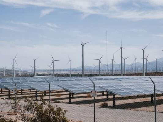 Solarpaneele auf einem sandigen Fläche Dahinter Windräder