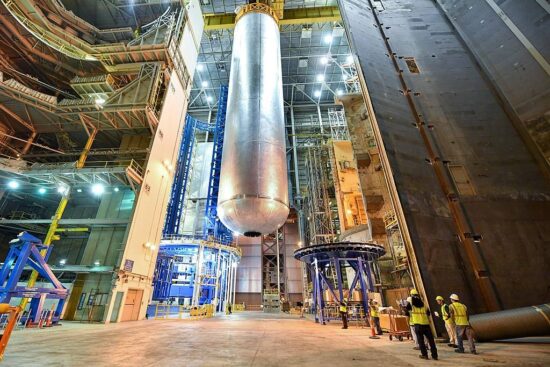 Ein riesiger zylindrischer Wasserstofftank wird mit einem Kran durch eine Industriehalle bewegt
