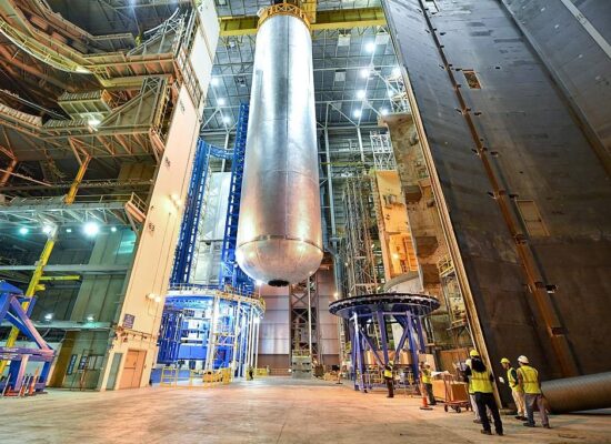 Ein riesiger, zylindrischer Wasserstofftank wird mit einem Kran durch eine Industriehalle bewegt.