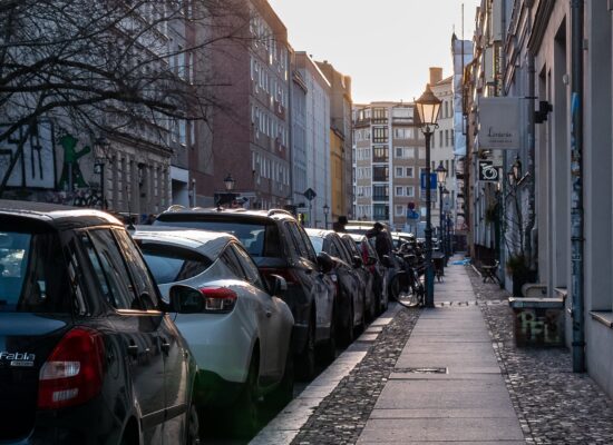 Eine Straße in der Stadt. Eine Reihe von Autos parkt neben einem engen Bürgersteig. Es sind kaum Menschen zu sehen.